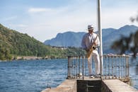 阳光明媚的日子里，群山环绕的湖边码头上，一个男人在演奏萨克斯管