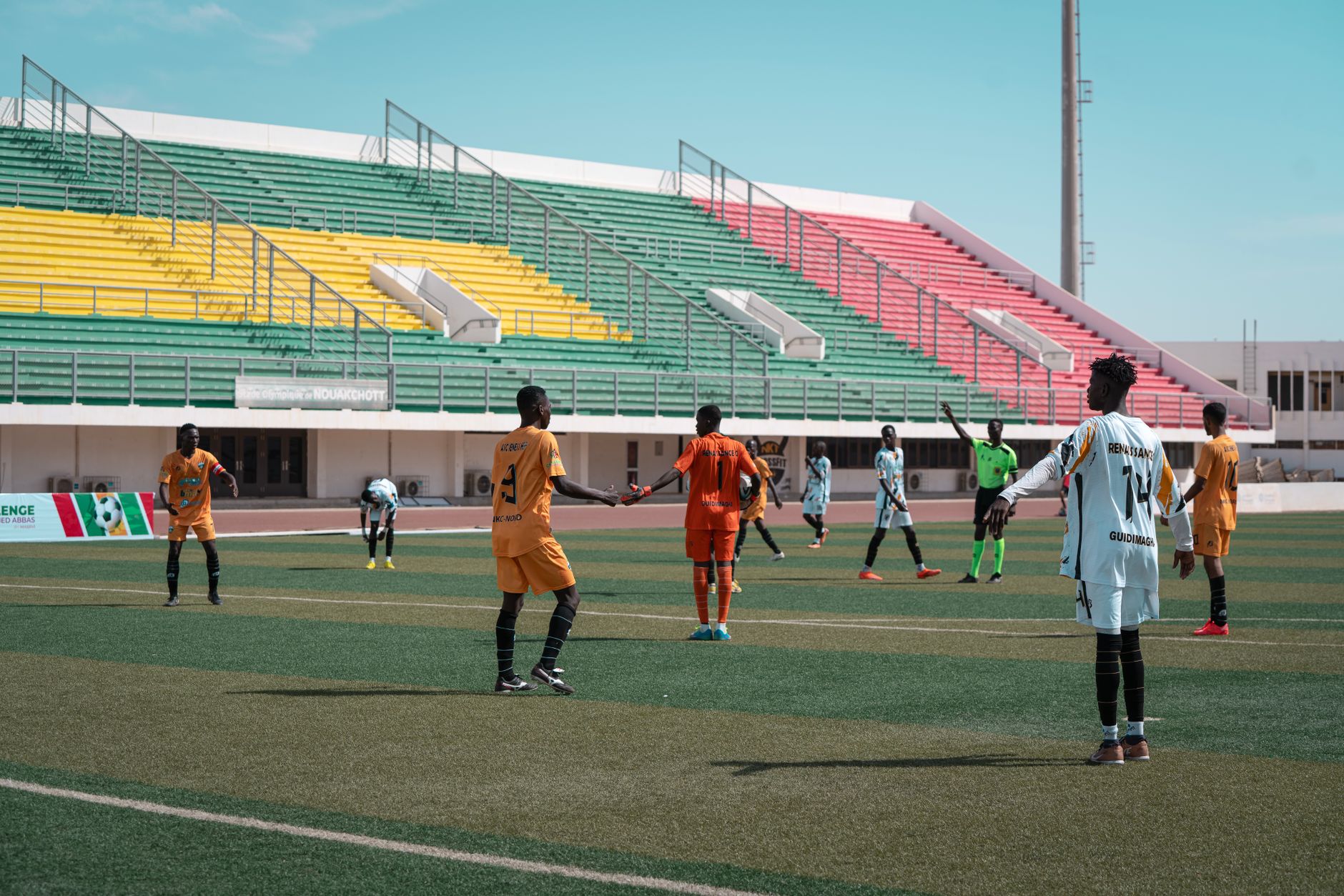 Energetic football match with players in orange and white, vibrant stadium backdrop.