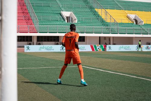 Free Soccer player in orange uniform on colorful stadium field during daytime game. Stock Photo