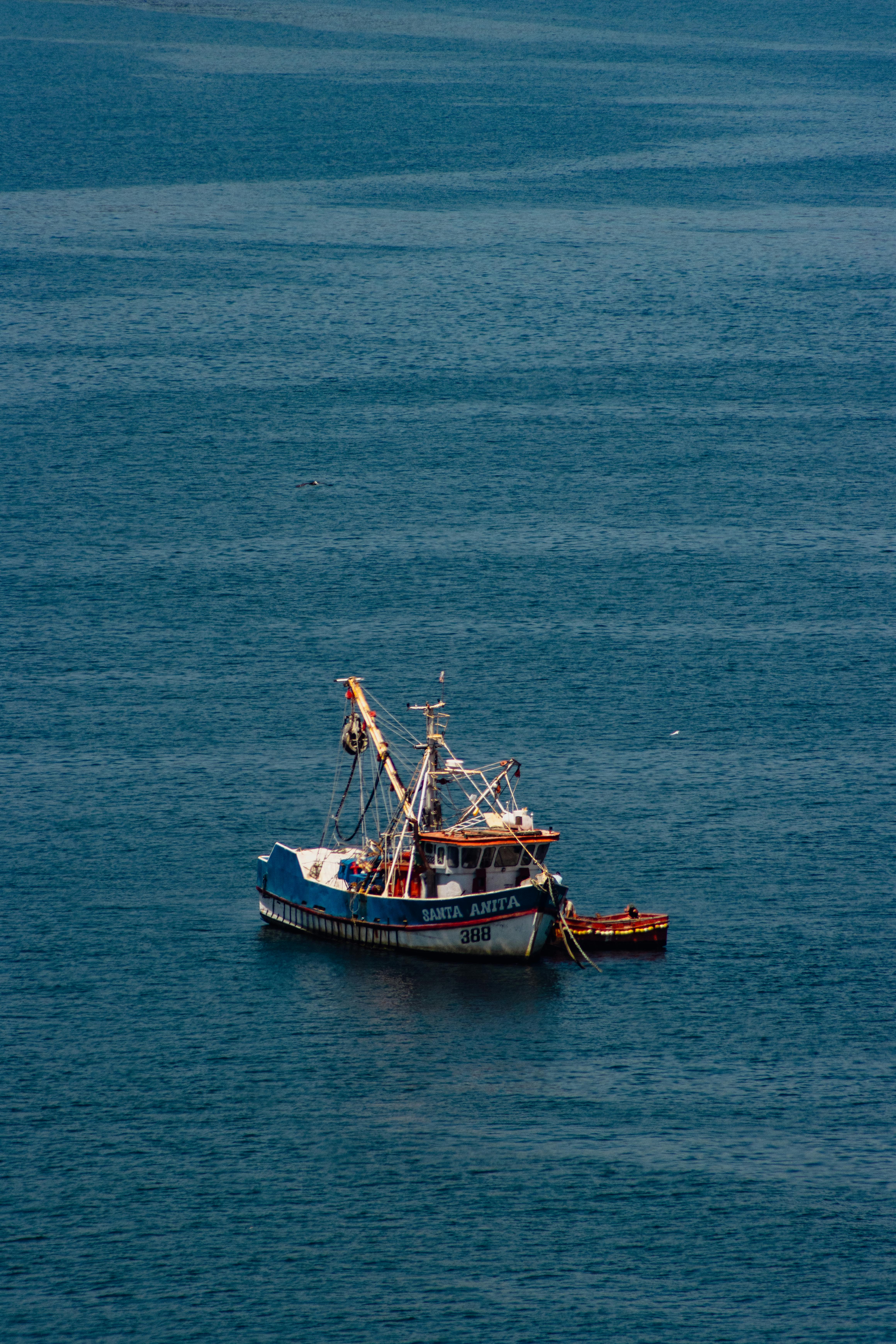 A fishing boat floats on the serene ocean off the coast of Lota, Chile, under a clear sky.