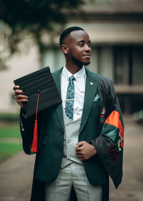 Free Smiling young graduate holding cap, wearing a gown, celebrating outdoors. Stock Photo
