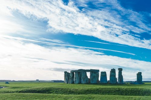 Free Stonehenge in Salisbury, England captured against a vivid blue sky and lush green fields. Stock Photo