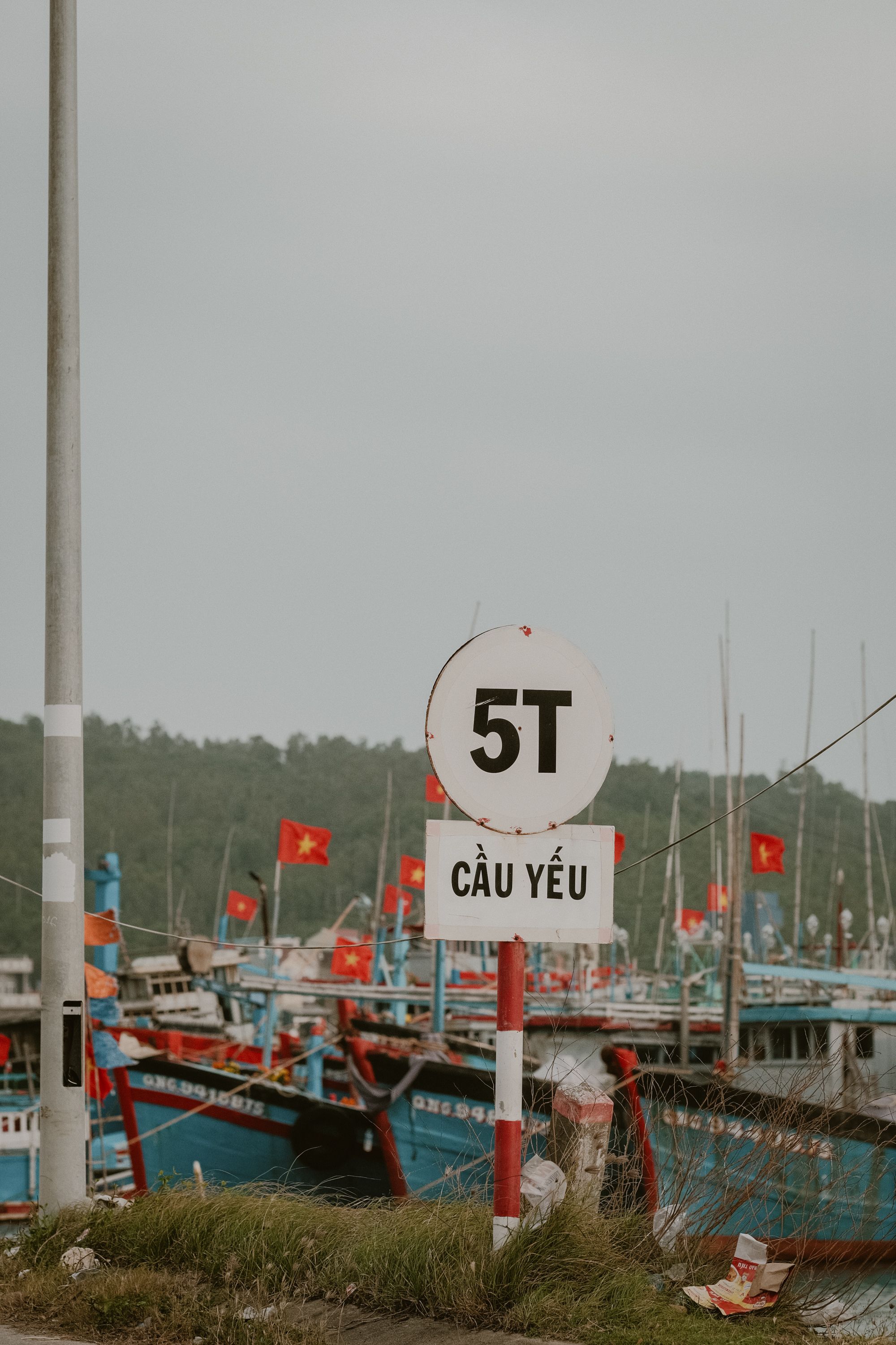 A fishing harbor in Vietnam with colorful boats and a Vietnamese road sign indicating weight limit.