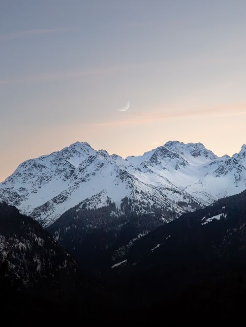Free Captivating view of snow-covered peaks in the Bavarian Alps under a crescent moon at sunset. Stock Photo