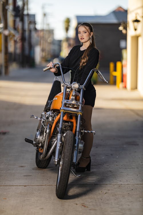 Woman in Black Mini Dress Stands by Orange Motorcycle