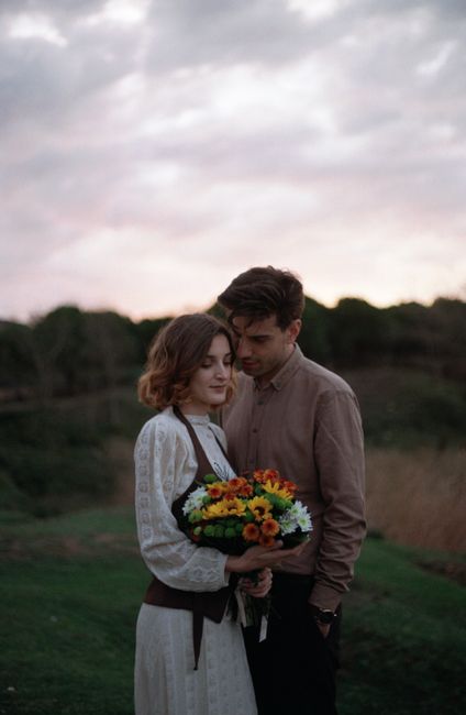 A romantic moment of a couple holding a bouquet of flowers in a serene meadow at sunset.