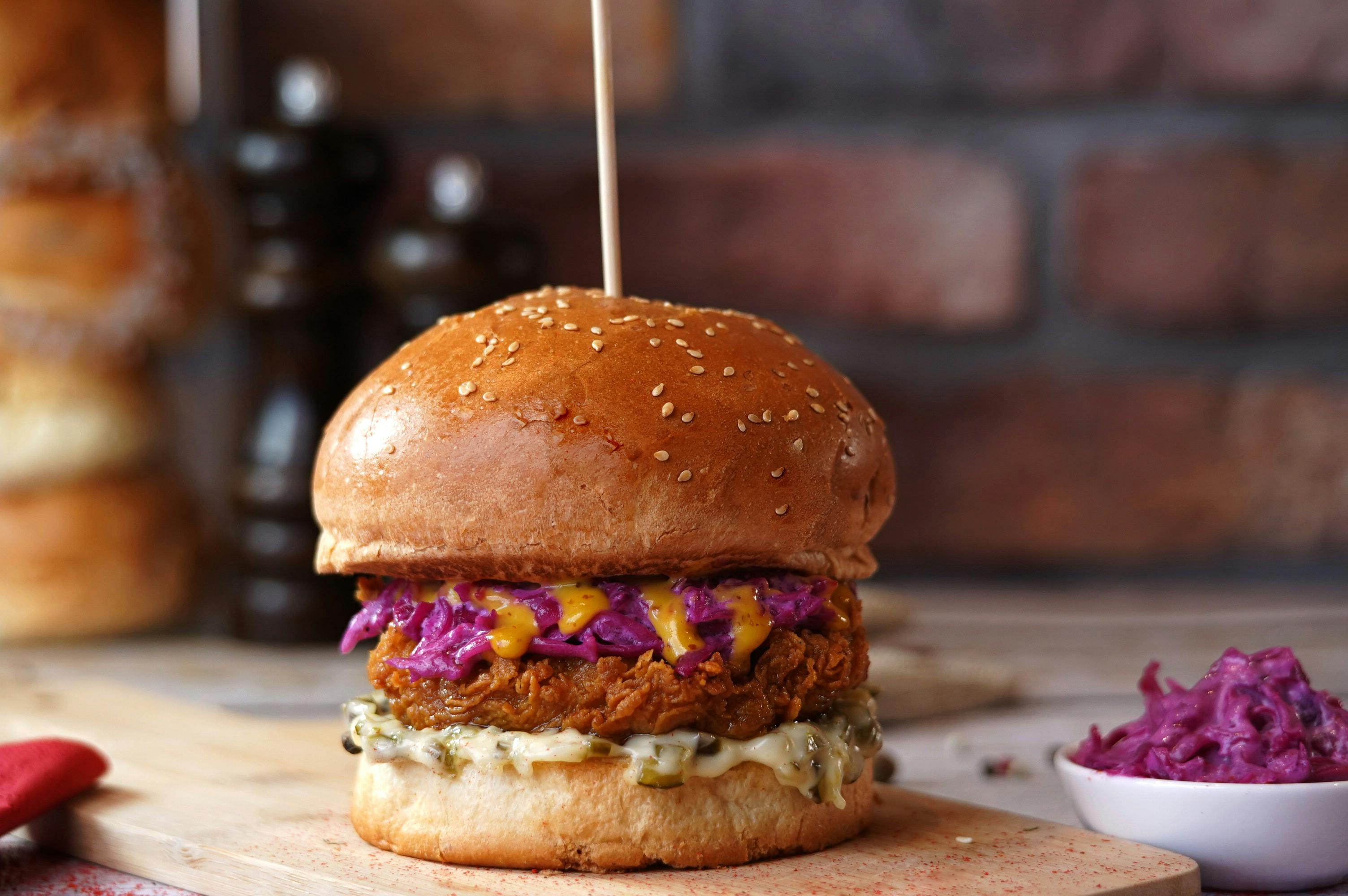 Korean fire chicken burger with glossy red gochujang glaze, pickled daikon slaw, and lettuce on a toasted brioche bun