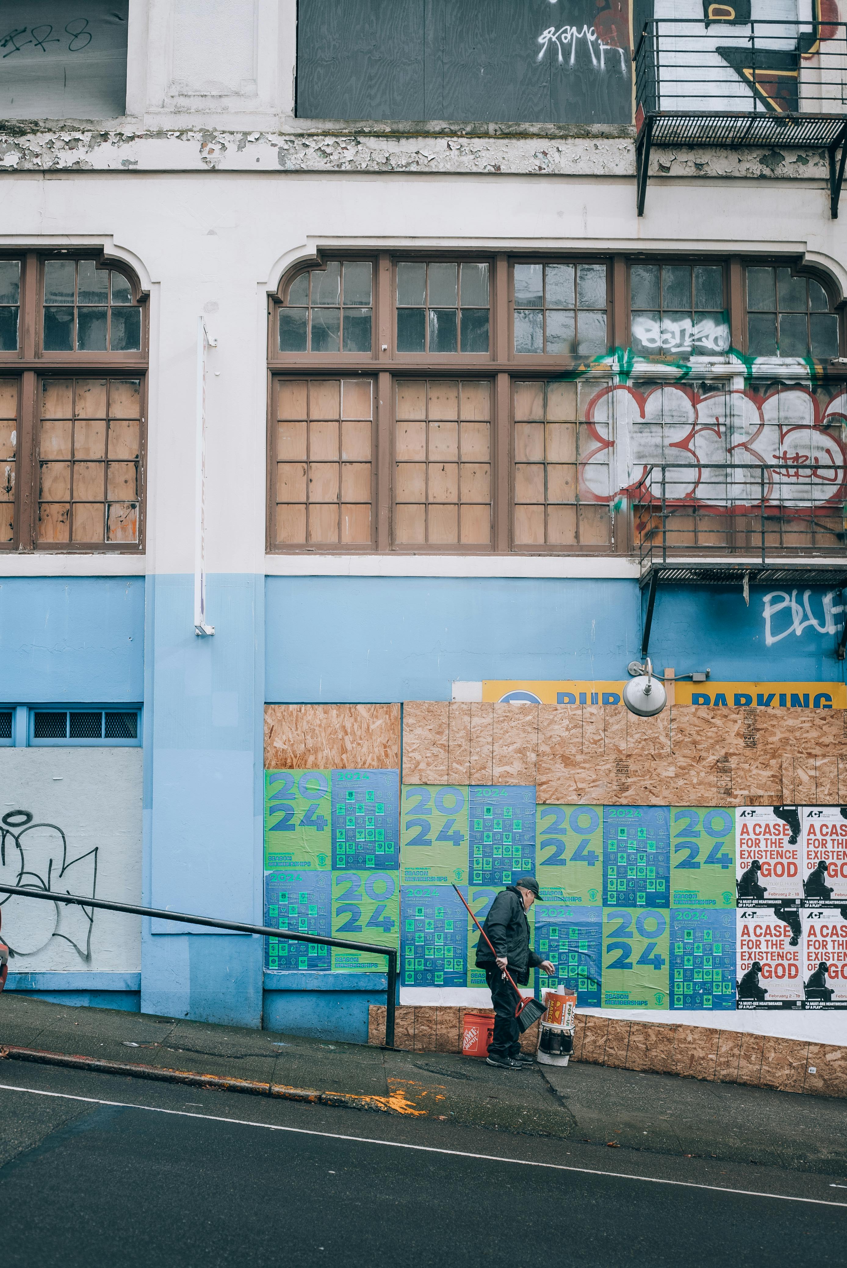 A man cleans a city sidewalk in front of a graffiti-covered building.