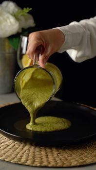 Close-up of broccoli soup being poured into a black bowl with elegant presentation.