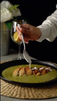 Close-up of a chef elegantly garnishing a chicken curry dish with cream.