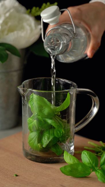 A small glass bottle of clear simple syrup next to a spoonful of granulated sugar and a measuring cup of water on a wooden counter.