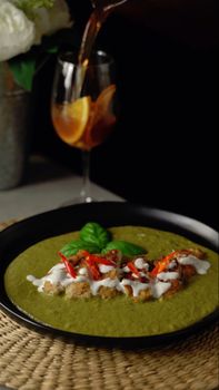 Close-up of gourmet broccoli soup garnished with red peppers, basil, and cream.