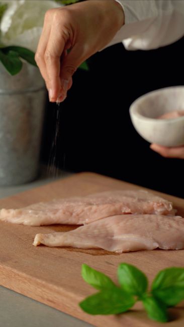 Three trimmed, boneless skinless chicken breast fillets arranged on a wooden cutting board next to a chef's knife.