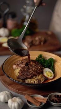 Close-up of beef ramen with broth, egg, and greens in a cozy setting.