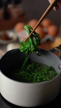 Cooked broccolini lifted with chopsticks from pot, showcasing fresh vegetable preparation.