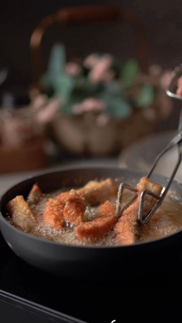 Golden, bubbly beer-battered fish fillets draining on a wire rack next to a bowl of leftover batter and a bottle of beer.