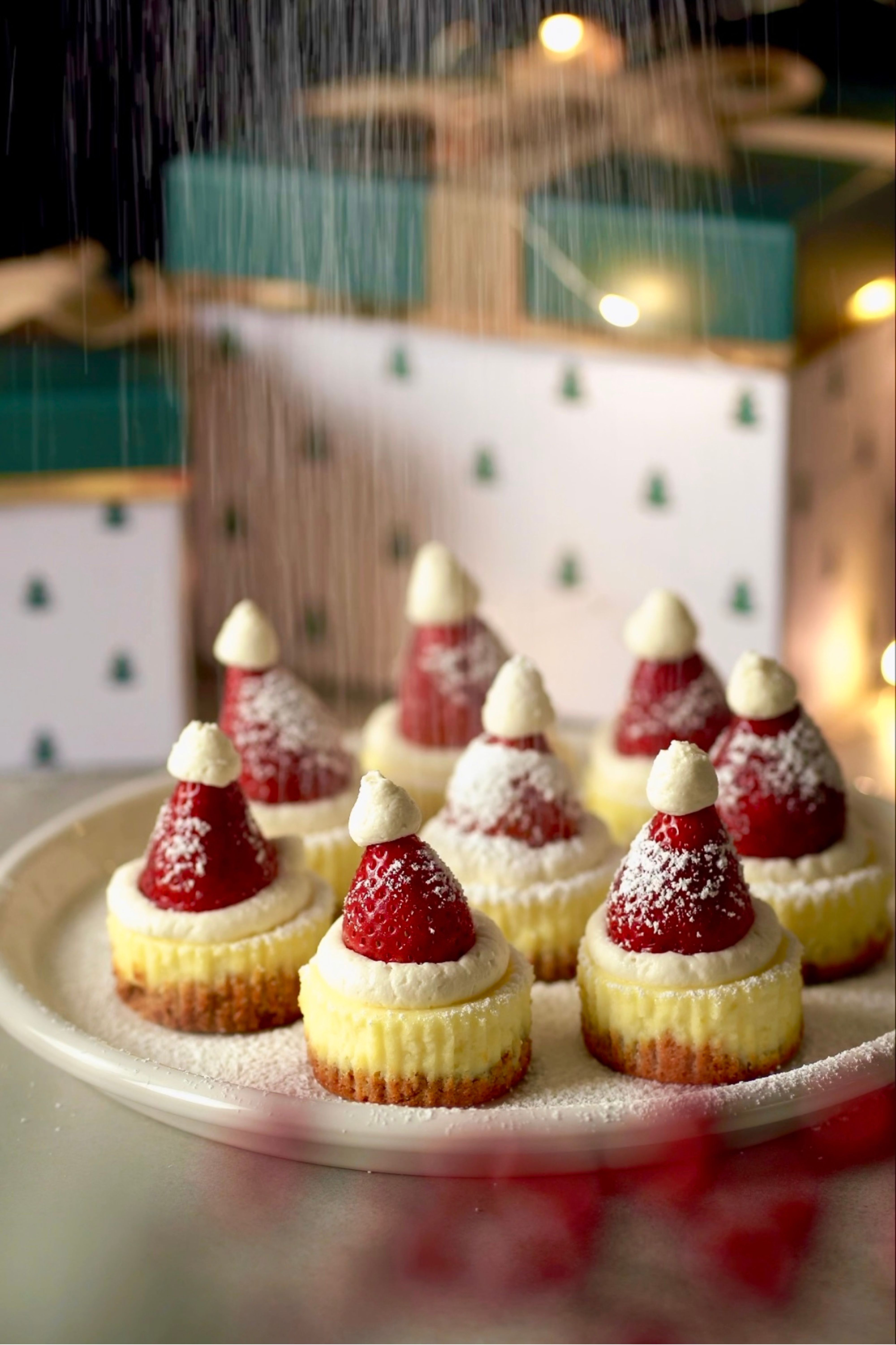 Christmas-themed mini cheesecakes with strawberry Santa hats and powdered sugar in a cozy holiday setting.