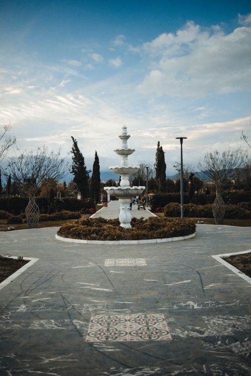 Free A beautiful marble fountain in a serene park with an overcast sky. Stock Photo
