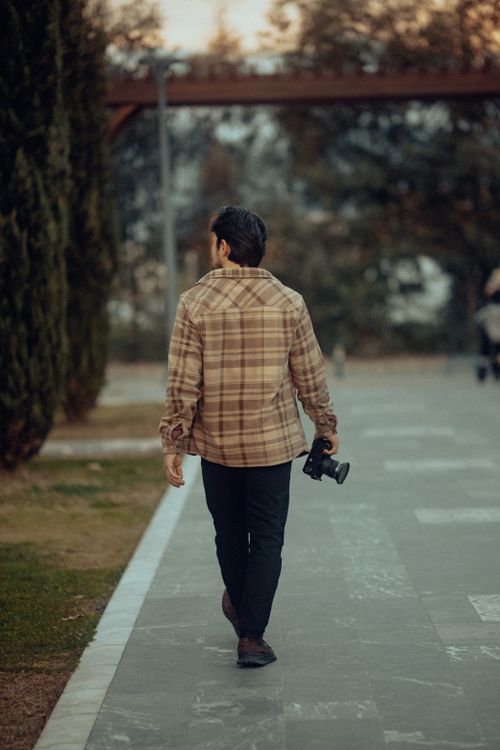 Free A man holding a camera walks through an urban park, showcasing a serene outdoor setting. Stock Photo