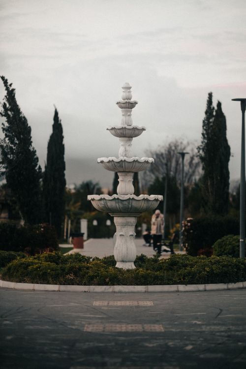Free A beautiful fountain surrounded by lush greenery in a serene urban park setting. Stock Photo