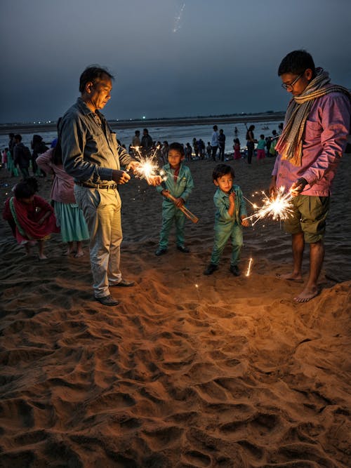 Men and Children Celebrating with Sparkles in their Hands on a Beach at Dusk 