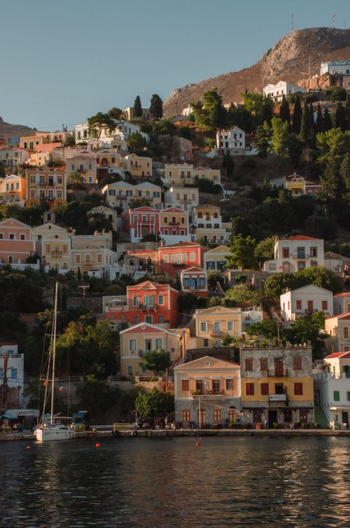 Free Panoramic view of Symi's vibrant hillside houses and tranquil sea, embodying Greek island beauty. Stock Photo