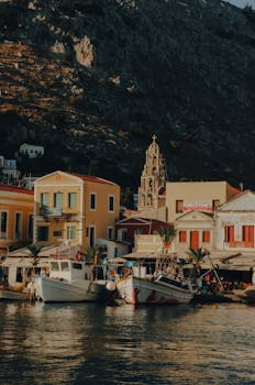 Scenic view of a Greek town with colorful buildings, moored boats, and a bell tower.