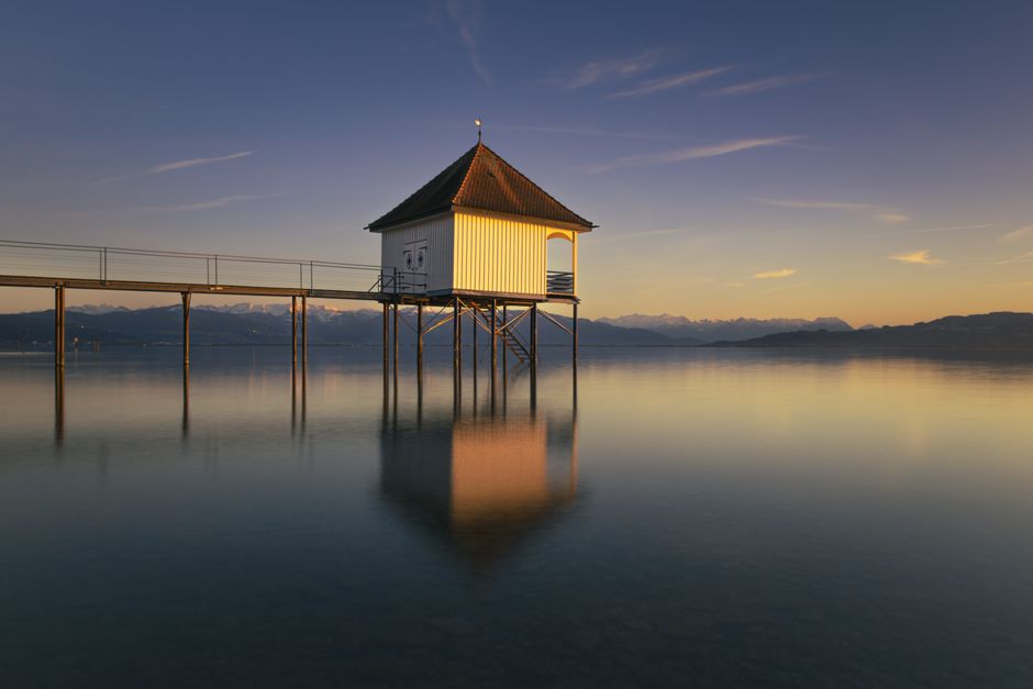 A tranquil pier house reflected in calm ocean waters during sunset, capturing a serene seascape.