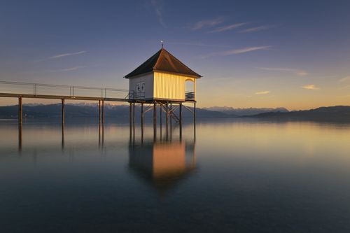 Free A tranquil pier house reflected in calm ocean waters during sunset, capturing a serene seascape. Stock Photo