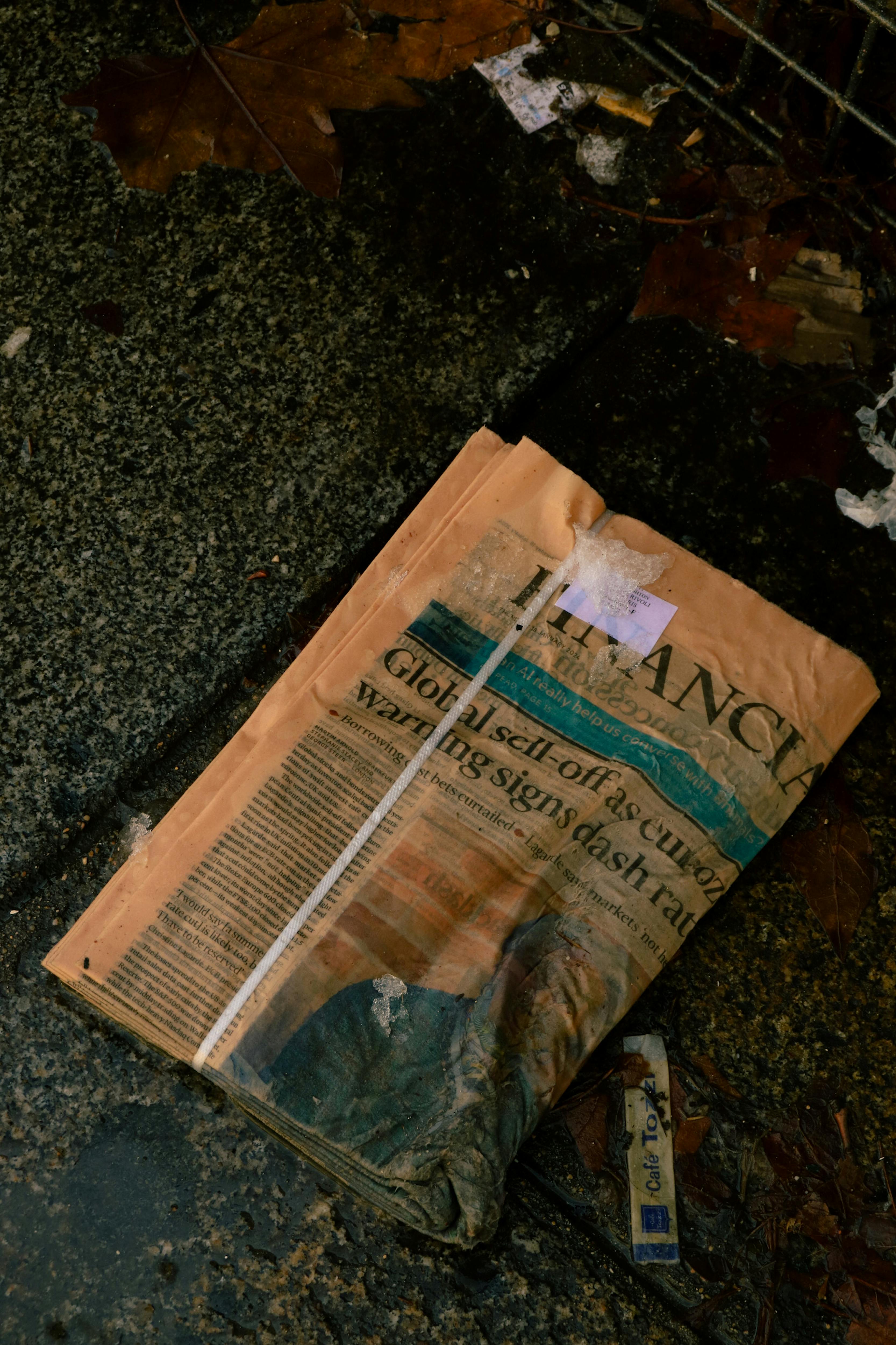 a newspaper laying on the ground next to a trash can