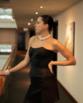Stylish woman in black corset dress with pearls, exuding elegance and glamour indoors.