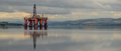 An offshore oil platform sits on calm waters beneath heavy, stormy grey clouds.