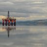 An offshore oil platform sits on calm waters beneath heavy, stormy grey clouds.