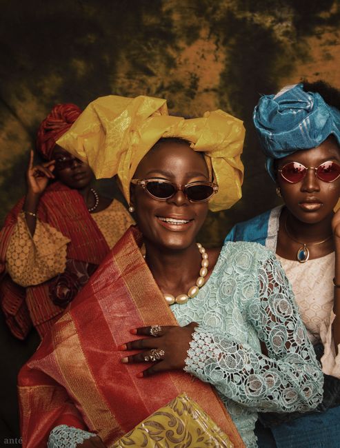 A joyful group of African women in colorful traditional clothing, smiling and wearing hats and sunglasses.