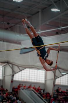 Captivating shot of a male pole vaulter soaring mid-air in a sports facility.