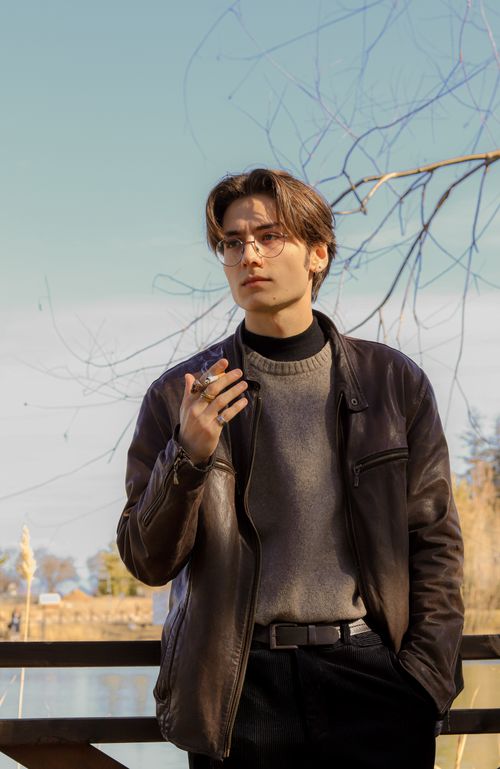 Free Stylish man wearing a leather jacket and eyeglasses, standing outdoors on a sunny day. Stock Photo