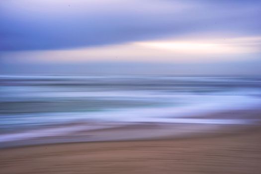 Serene beach scene with ocean waves and sky in motion blur captured during sunset.