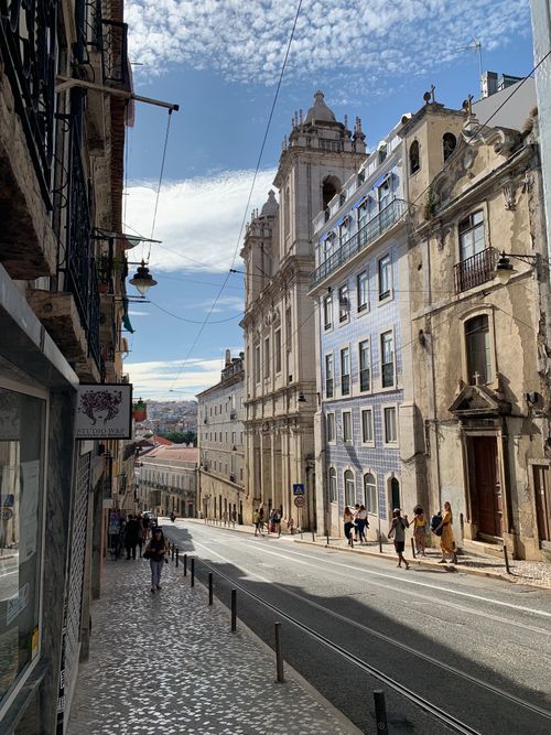 Free Explore a sunny Lisbon street lined with traditional buildings, capturing urban life and history. Stock Photo