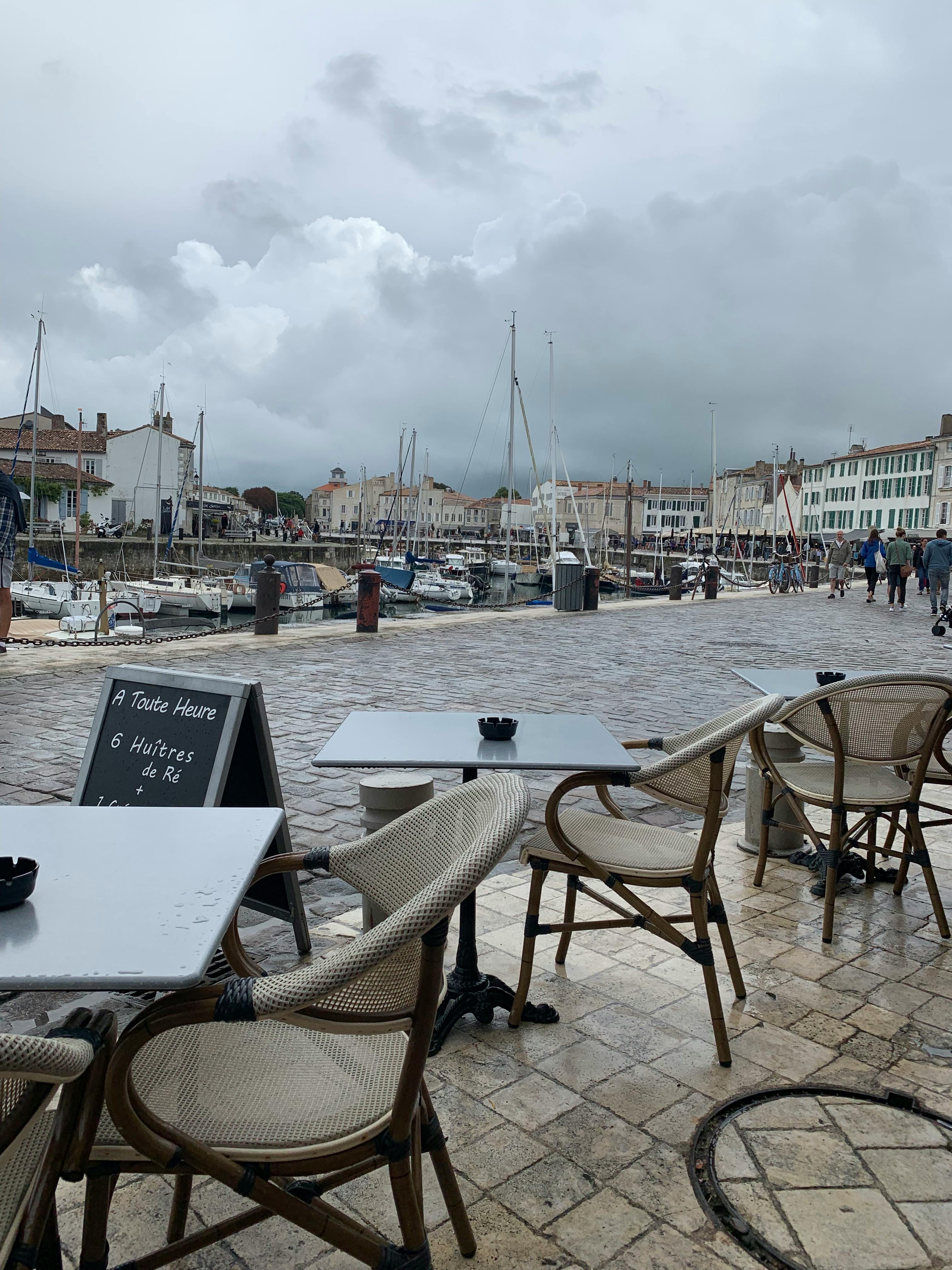 Outdoor cafe seating with a view of the harbor under a cloudy sky, offering a cozy dining atmosphere.