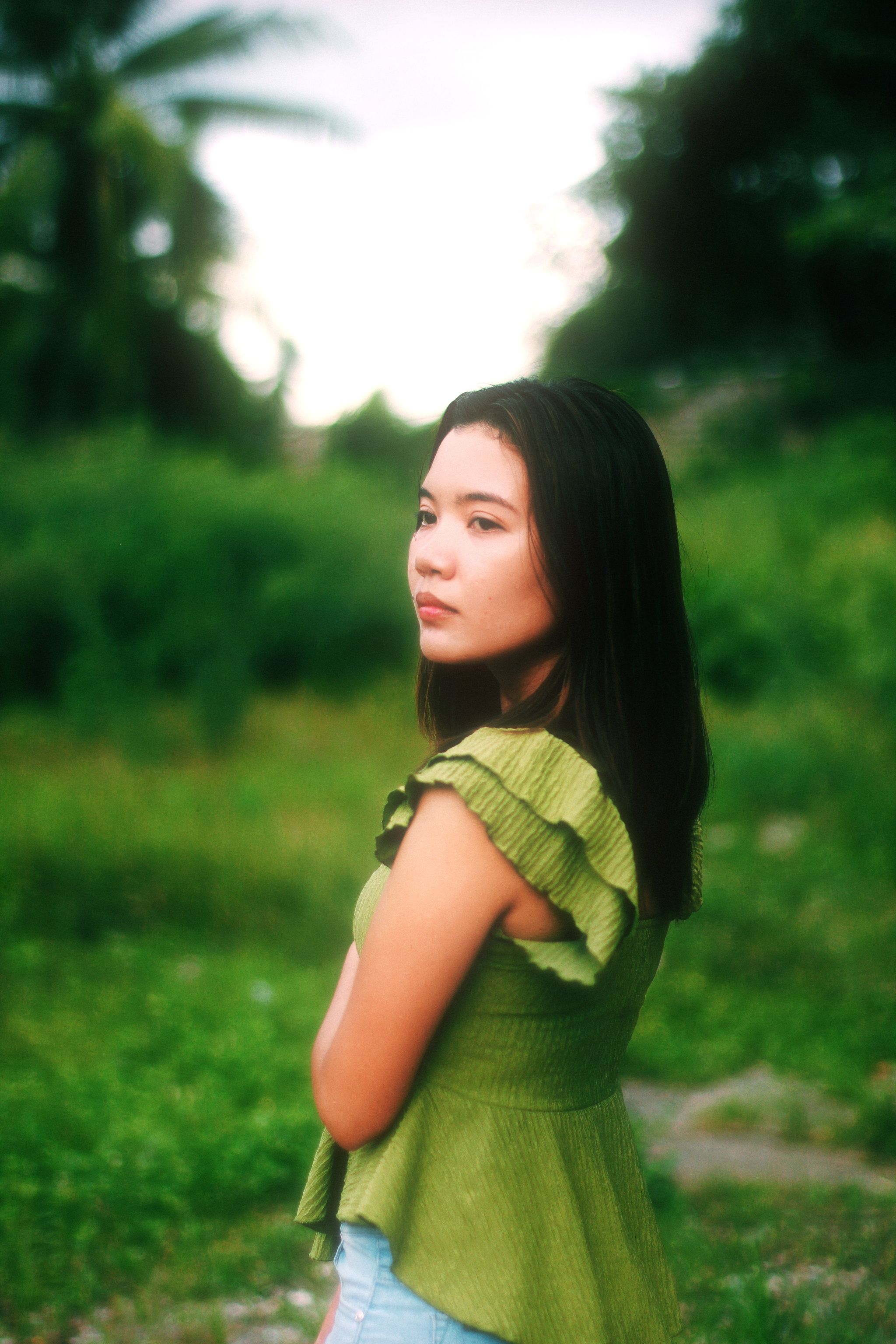 Young woman in a green blouse poses outdoors, showcasing fashion in nature.