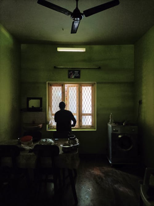 Person Standing in Dark Room and Looking through Window