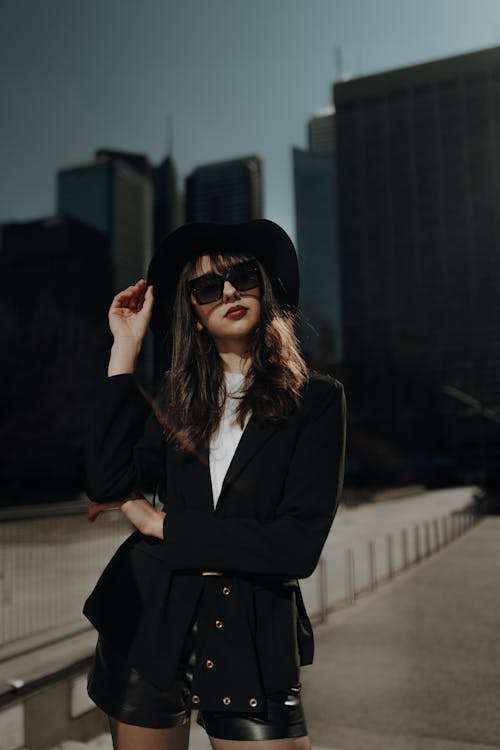 A woman in a hat and sunglasses is posing in front of a city