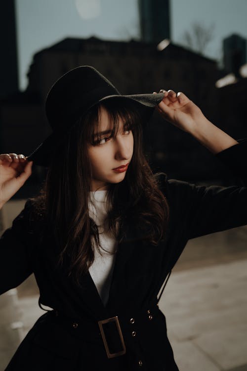 A woman in a hat and coat posing in front of a city