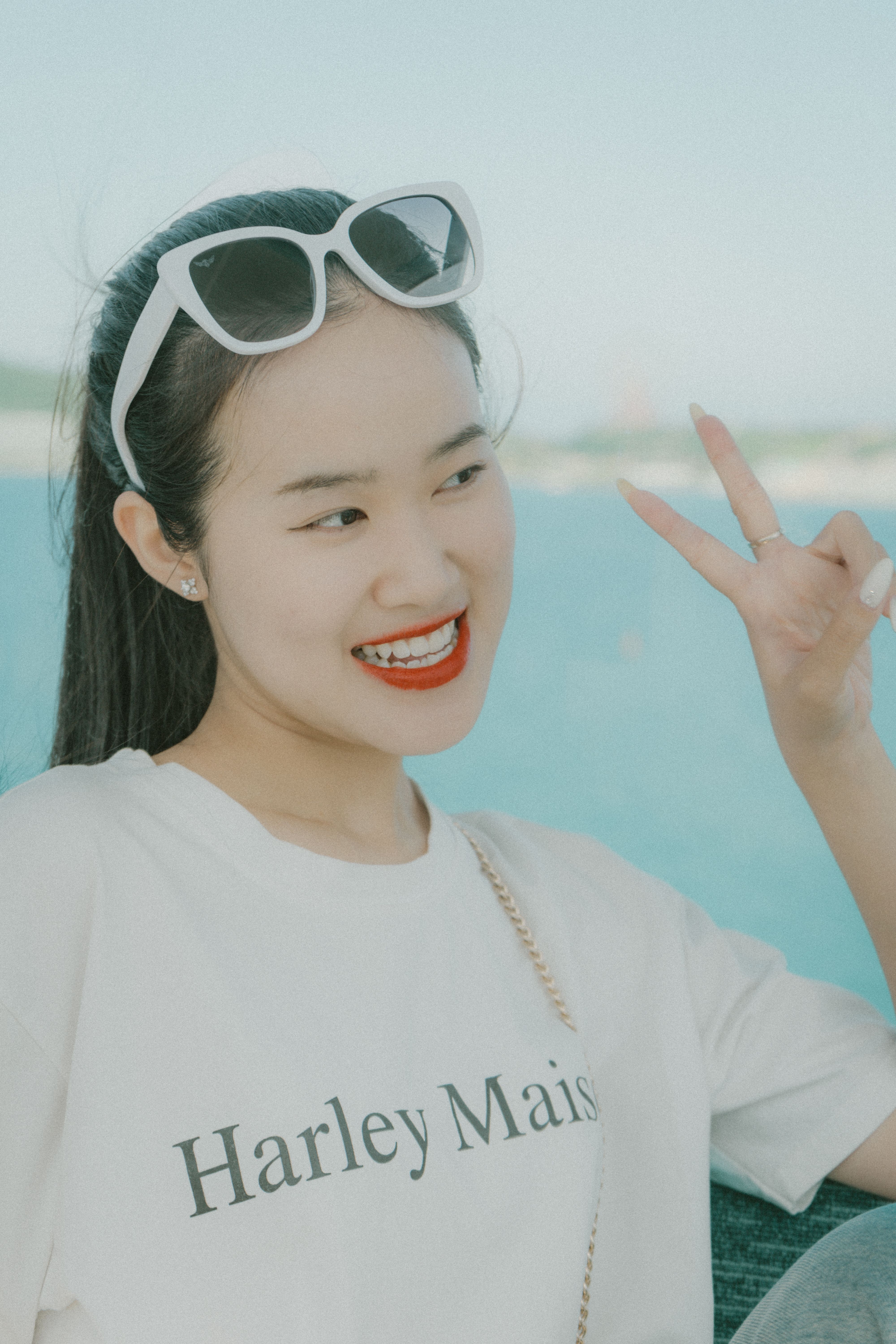 Stylish woman with sunglasses and a white t-shirt making a peace sign outdoors.