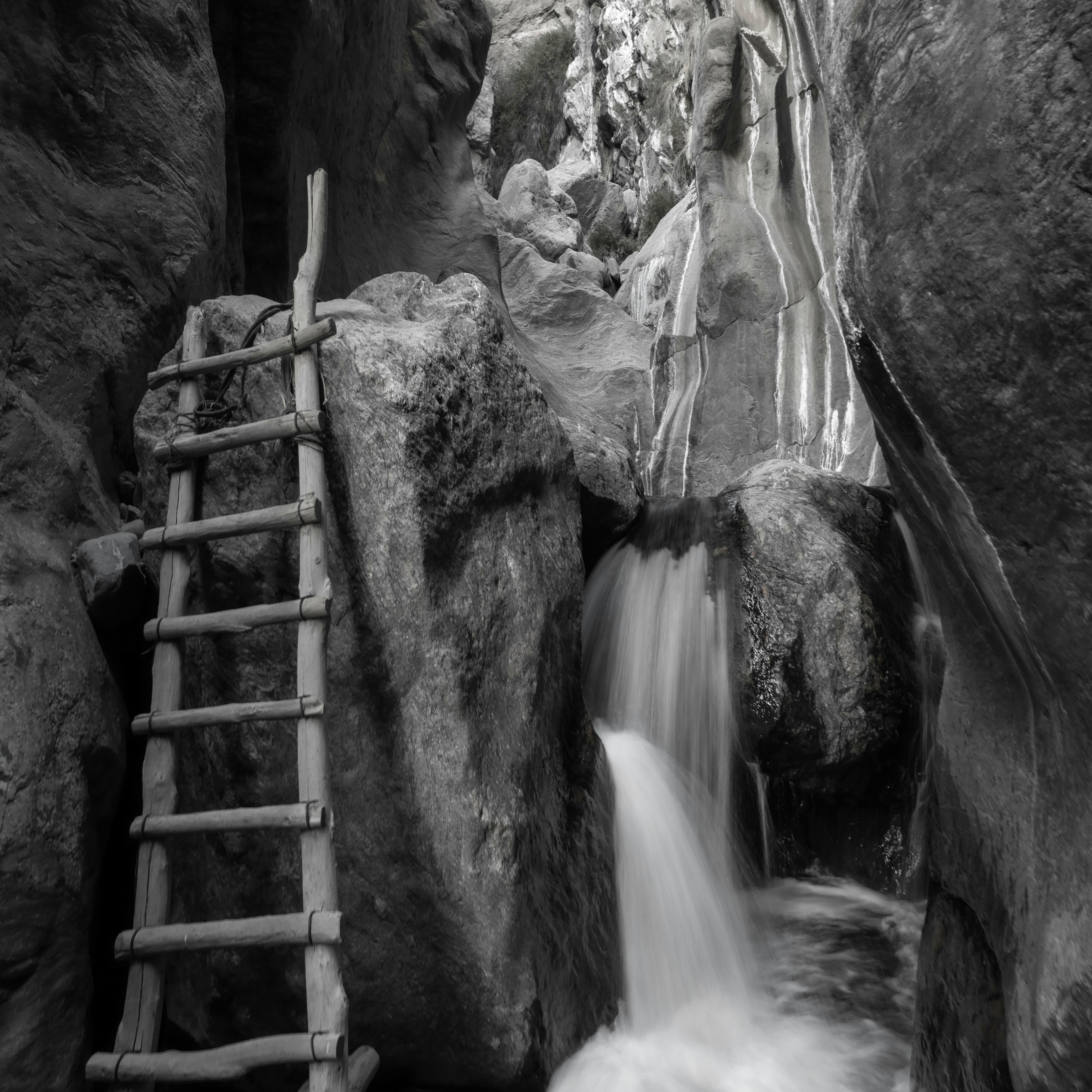 A wooden ladder beside a waterfall in a narrow canyon, capturing dramatic textures and natural beauty.