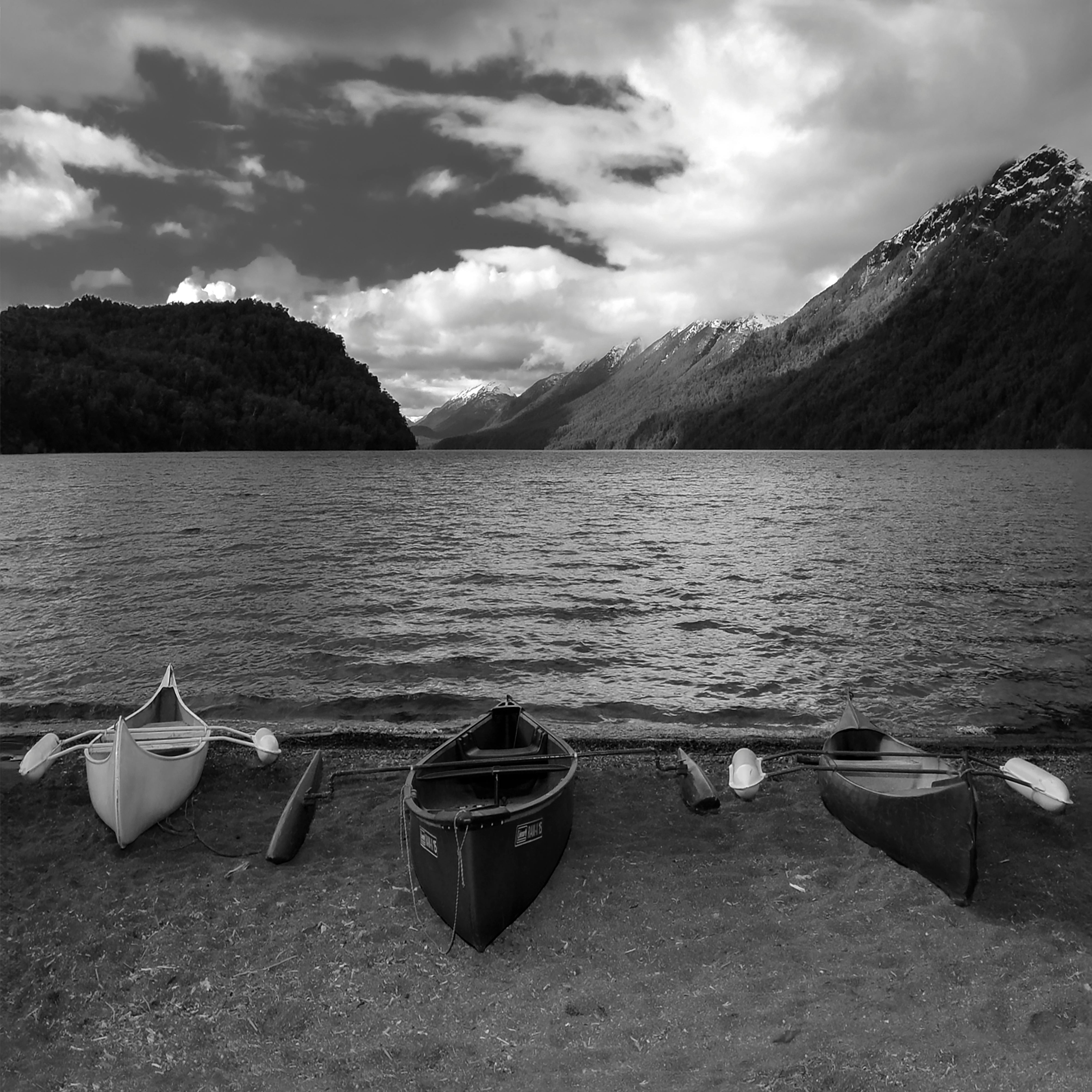 Black and white photo of a lake with canoes and mountain backdrop, creating a serene atmosphere.