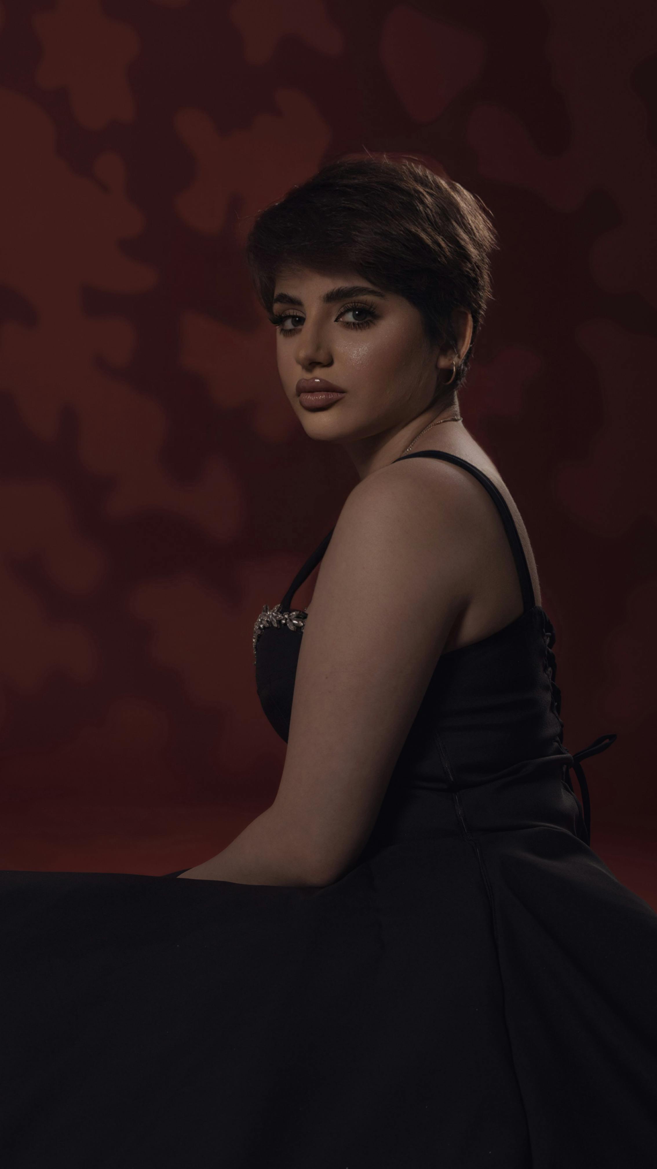 Studio portrait of a woman in black dress posing against a red background in a side view.