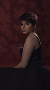 Studio portrait of a woman in black dress posing against a red background in a side view.