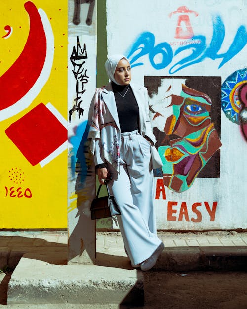 A woman in a hijab standing next to a wall with graffiti