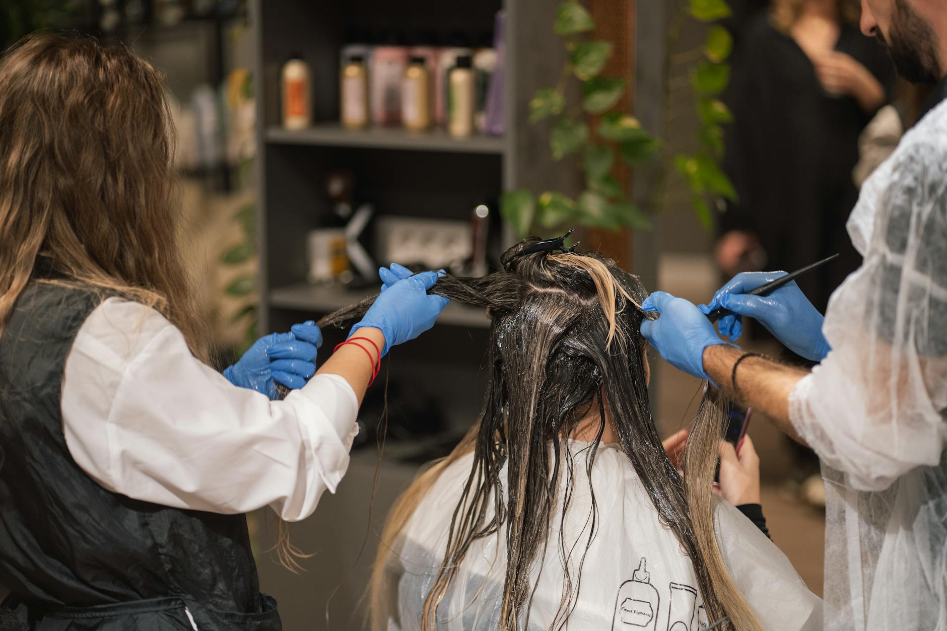 Hair care products and tools - professional stylists dyeing a woman's hair in a modern salon setting, showcasing teamwork ...